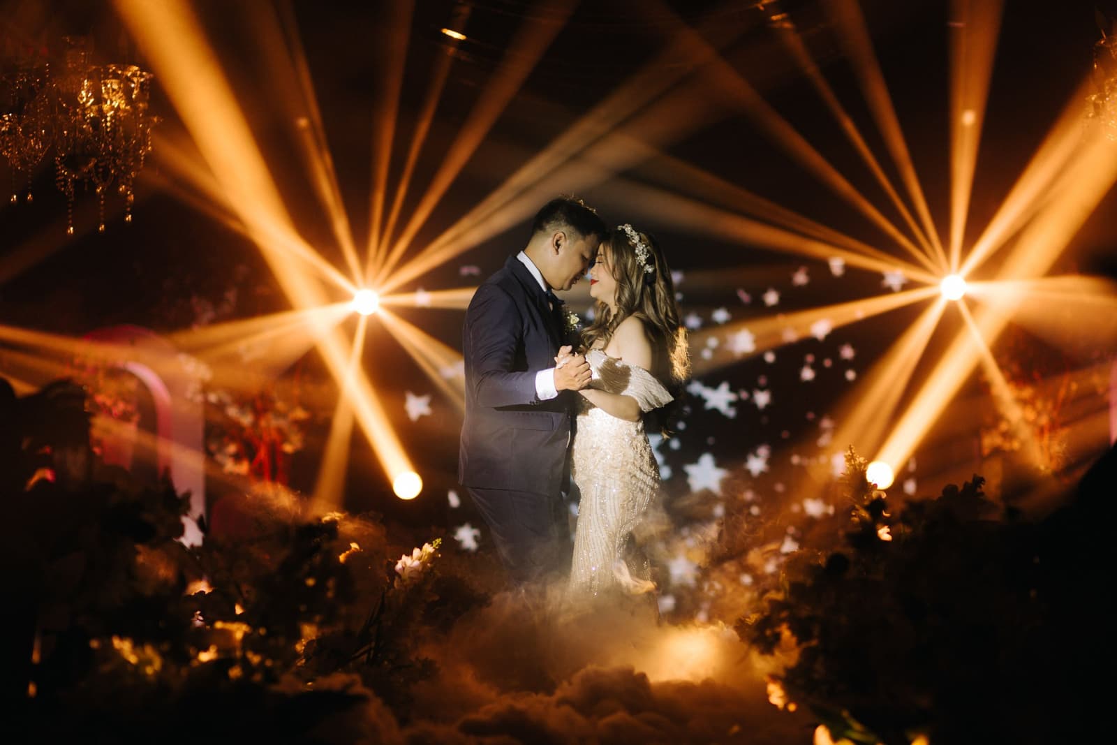 Couple dancing under warm gold stage lights at a wedding reception